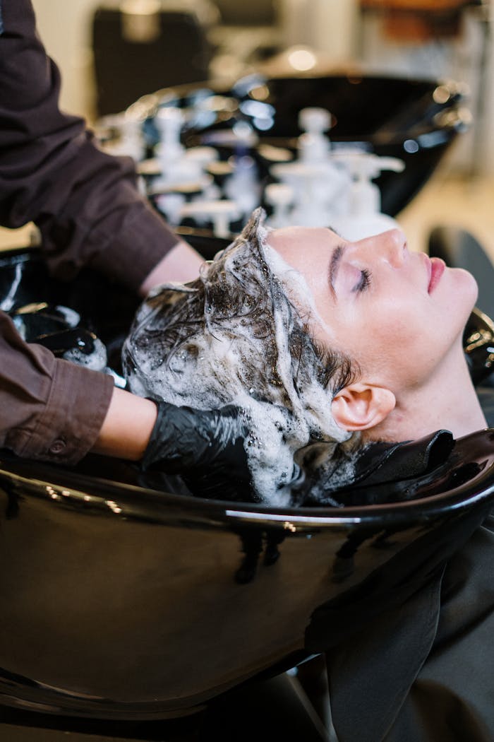 ours-journey Professional hair stylist washing woman's hair in a modern salon setting.